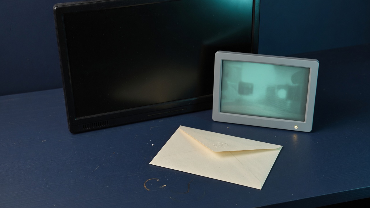 Two monitors on a navy desk, one dark and one glowing teal, with a cream envelope in front
