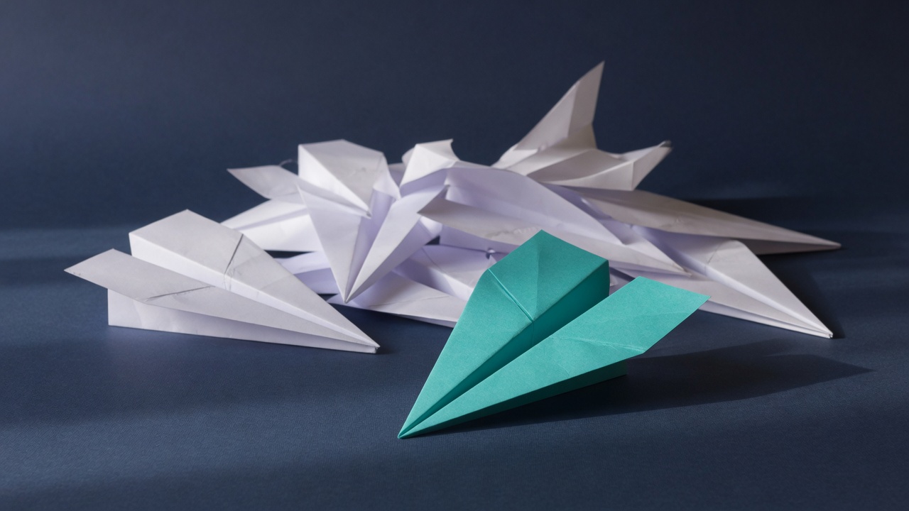 Several paper planes on a dark navy table, one of them teal