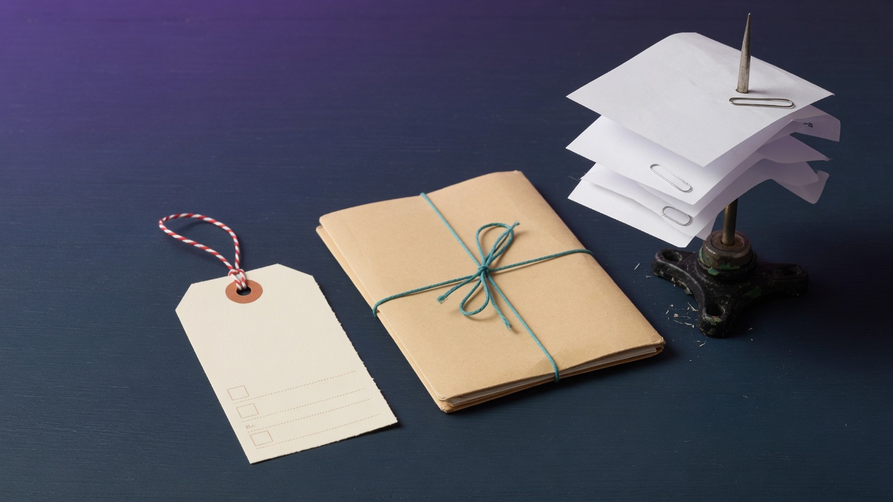 A blank price tag, a folder tied with teal cord, and a metal receipt spike on a dark navy desk